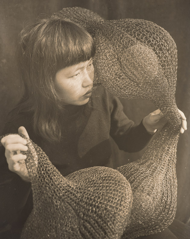 portrait of ruth asawa holding one of her scultpures and gazing into the distance
